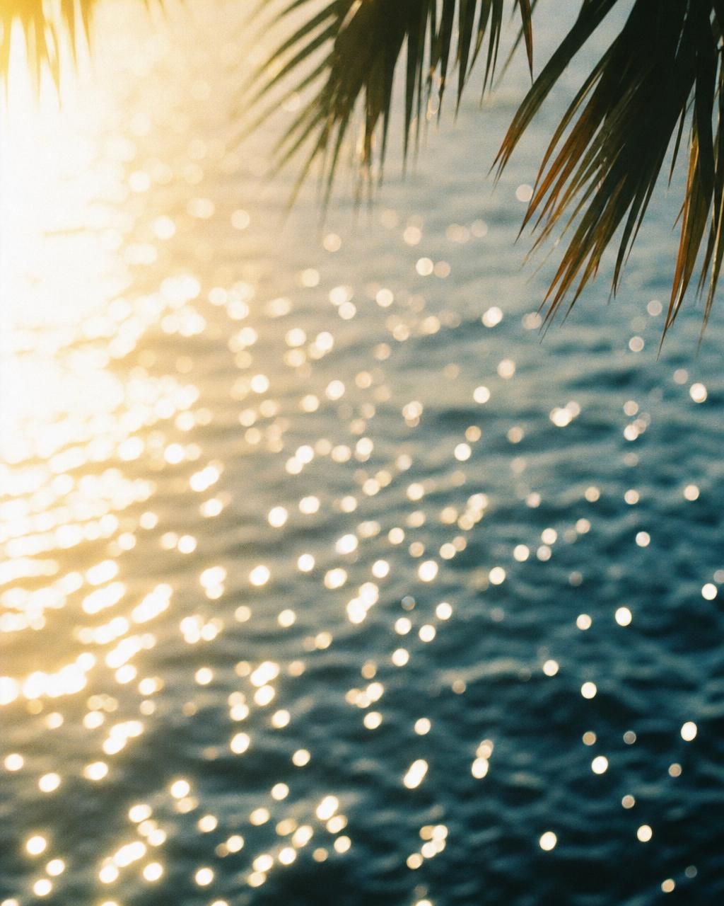 Sunlight scattering in silver-blue shimmer across rippling water beneath palm fronds.